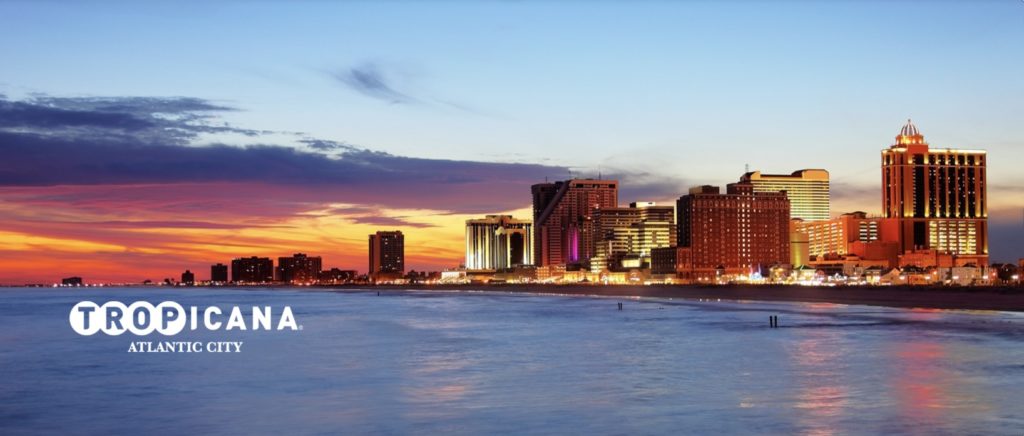 Image of the Atlantic City skyline and coast featuring the Tropicana. In the forefront of the image is "Tropicana Atlantic City." The sun is setting in the background.